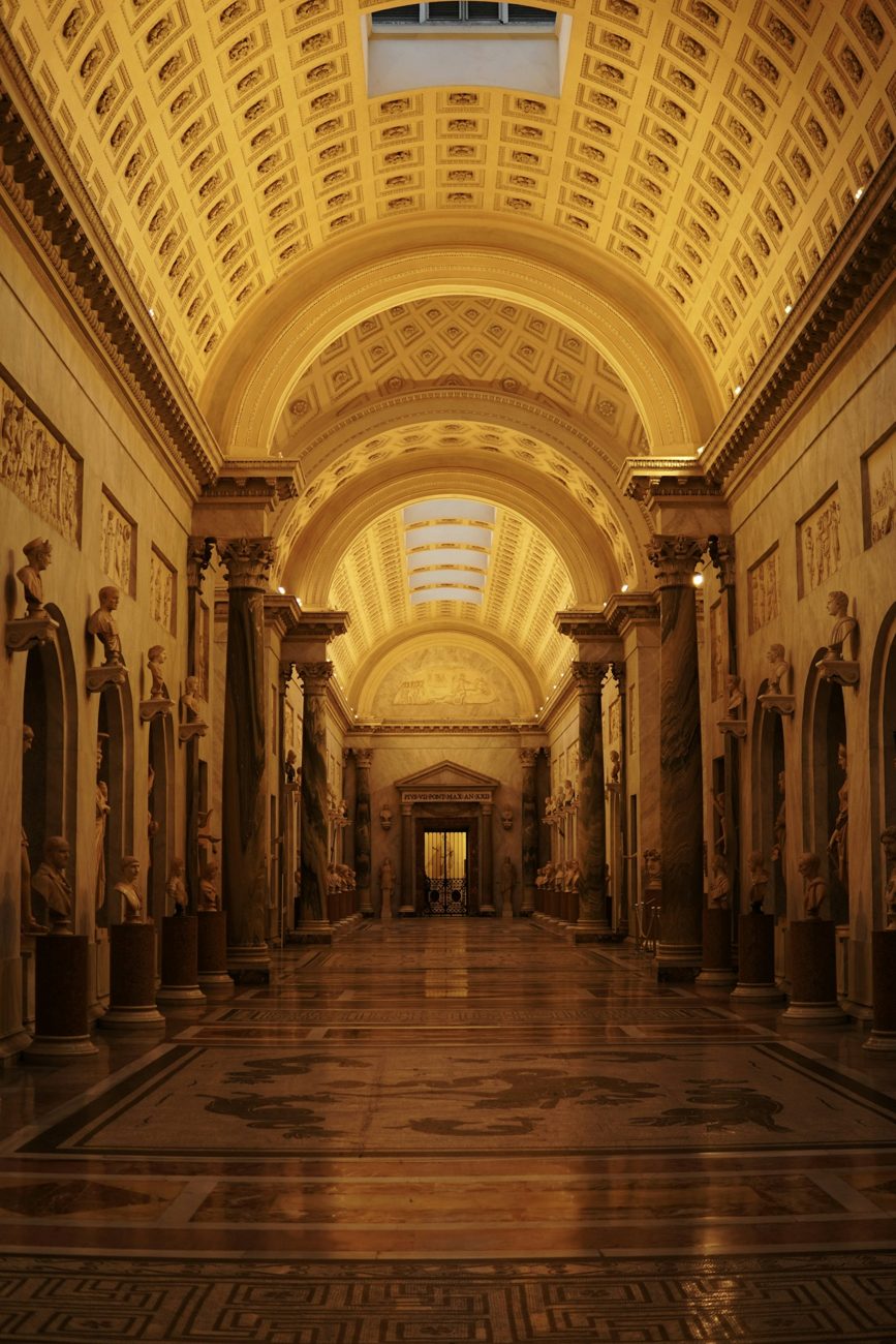 Classical sculpture gallery beneath an ornate coffered ceiling